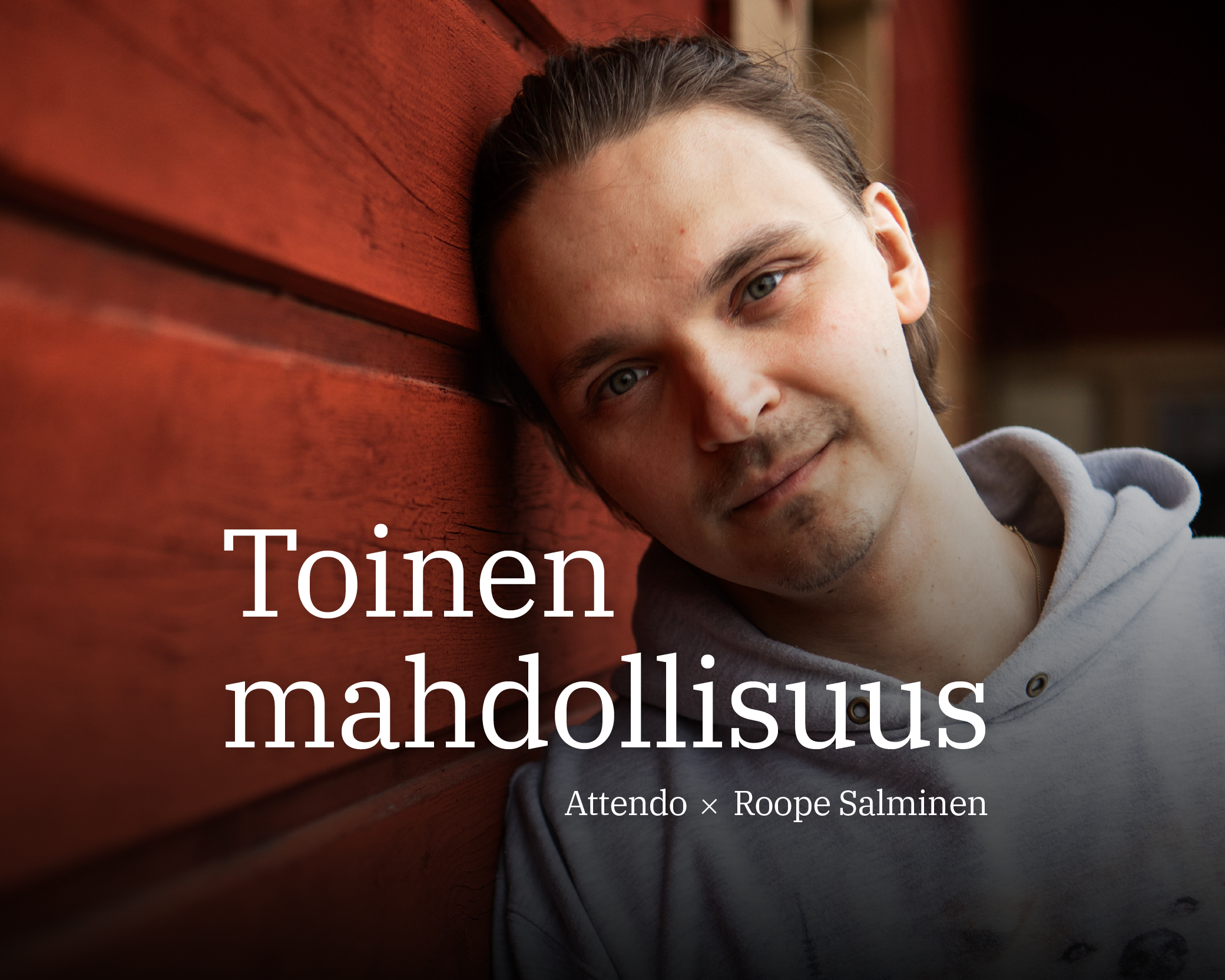 Roope nojaa punaiseen puuseinään, yllään harmaa huppari. Kuvassa tekstinä